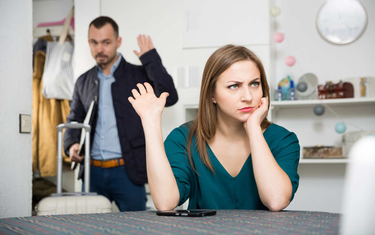 Man with suitcase leaving a distressed woman, symbolizing divorce and delays.