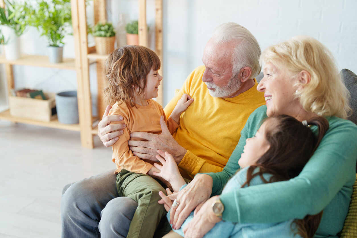 Grandparents embracing and playing with their two young grandchildren on a couch, symbolizing grandparents' visitation rights.