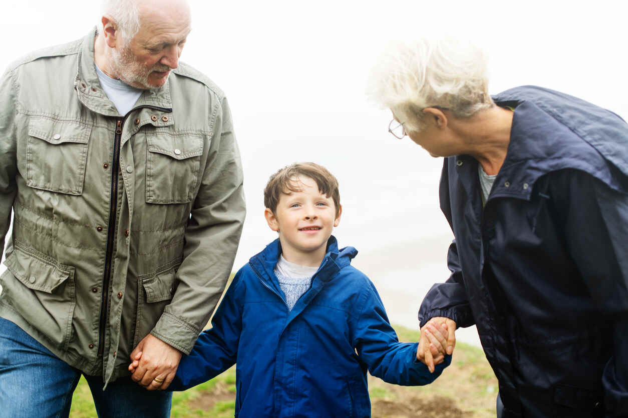 Grandparents holding hands with their smiling grandson, symbolizing legal guardianship.