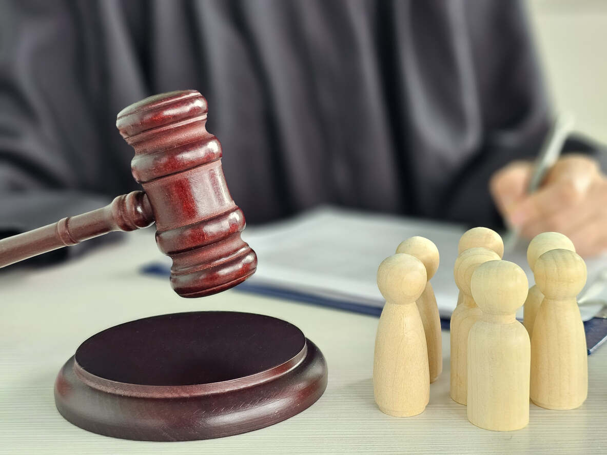 A judge's gavel next to wooden figures representing a family, with a person writing in the background, symbolizing child custody legal matters.
